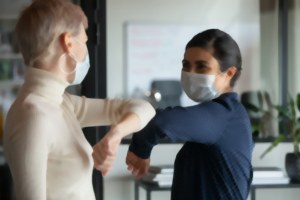Due donne con mascherina si salutano col gomito, immagine sfocata Covid